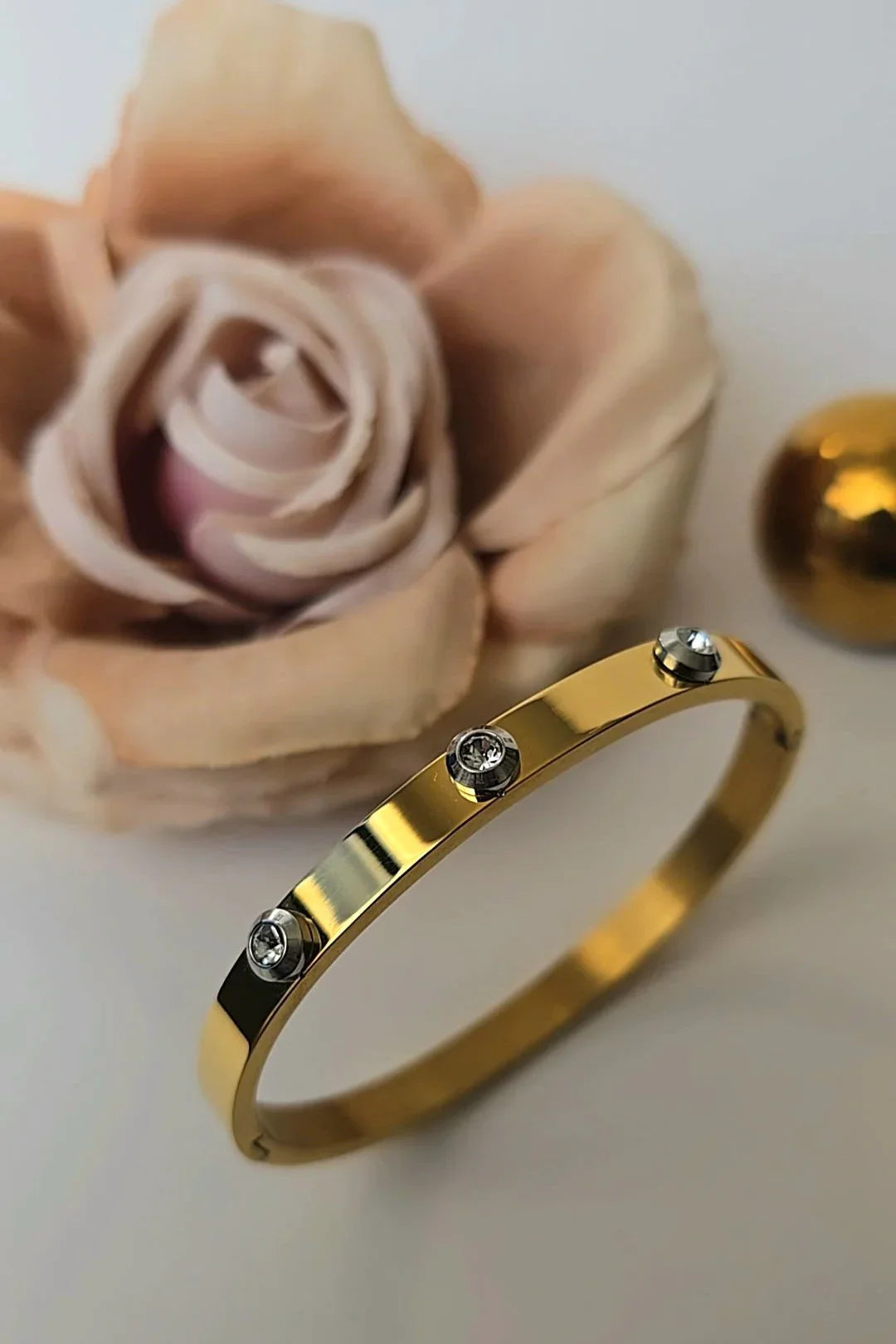 Gold bracelet with clear gemstones from Blissbymi, styled with a soft pink rose background.