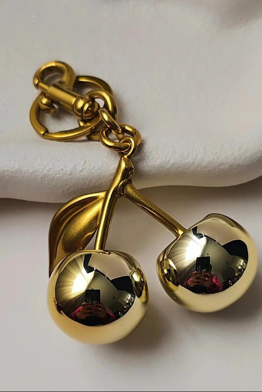 Gold cherry pendant keychain Bliss Bymi jewelry on white fabric background