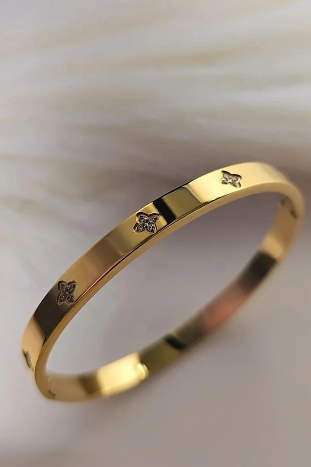 Gold bracelet with small diamond accents and floral motifs on soft background, Blissbymi jewelry