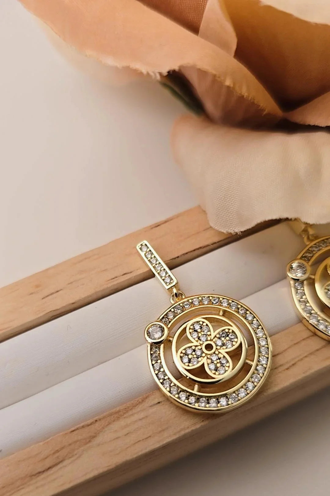 Gold crystal studded Blissbymi round dangle earring with floral design displayed on wood