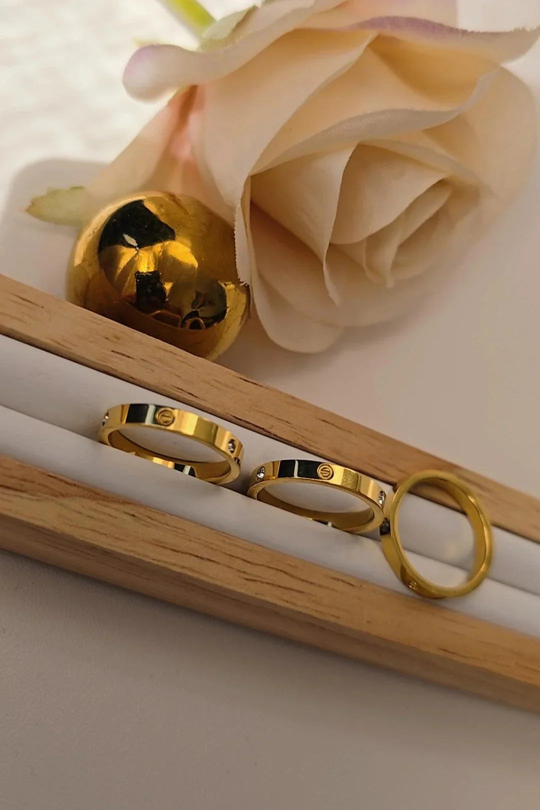 Gold rings from Blissbymi displayed with a rose and gold sphere in a wooden holder