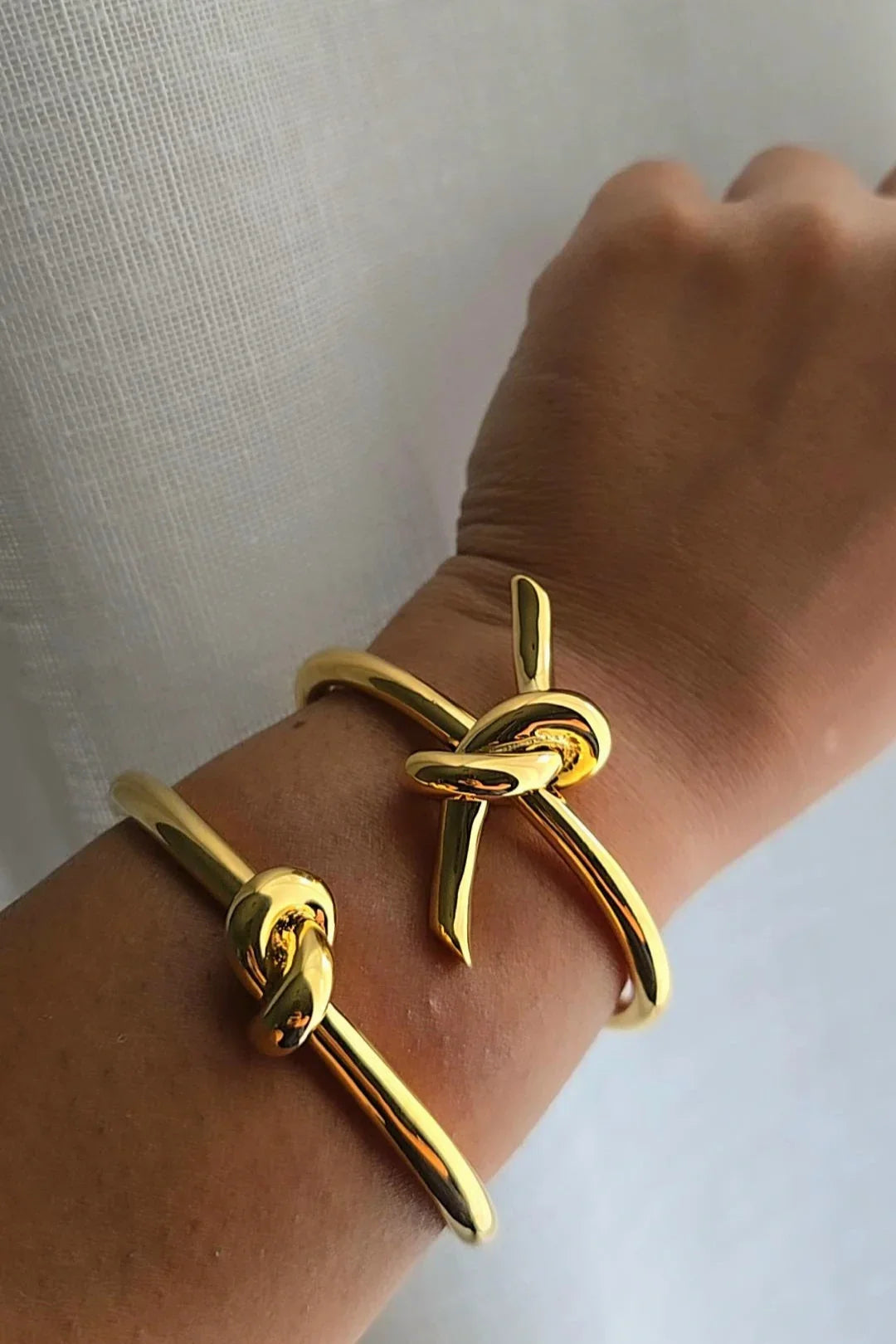 Gold knot bracelets from Bliss Bymi on wrist, minimalist jewelry against light background