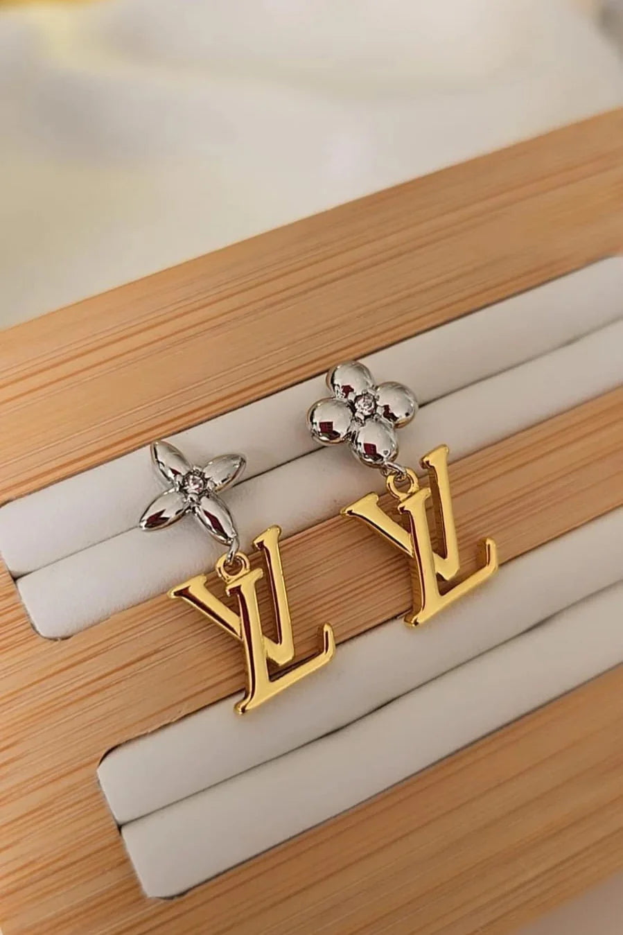 Gold and silver LV letter drop earrings by Blissbymi displayed on a wooden jewelry stand.