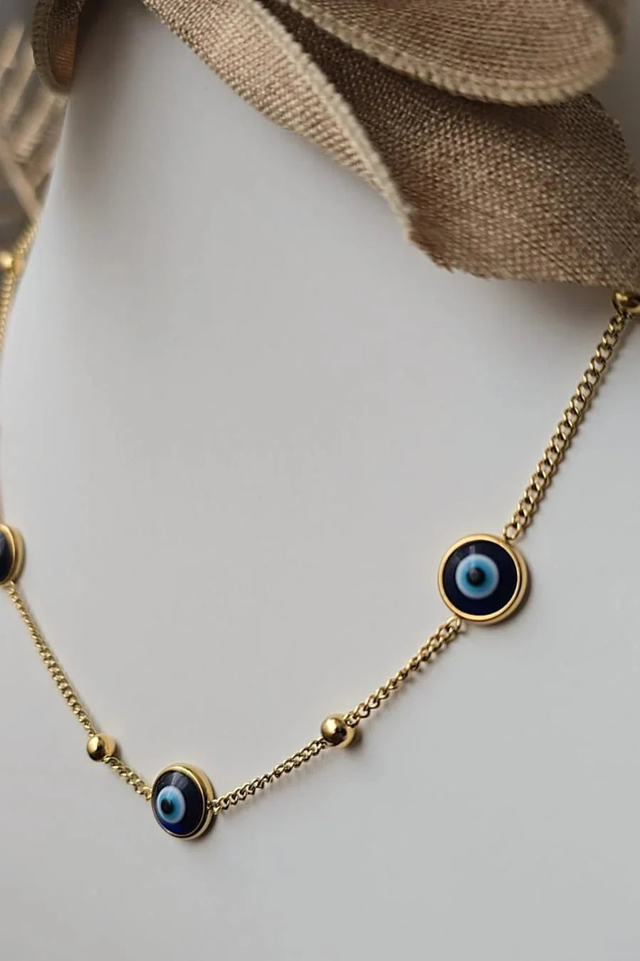 Gold chain necklace with blue evil eye charms by Blissbymi, displayed on a white bust