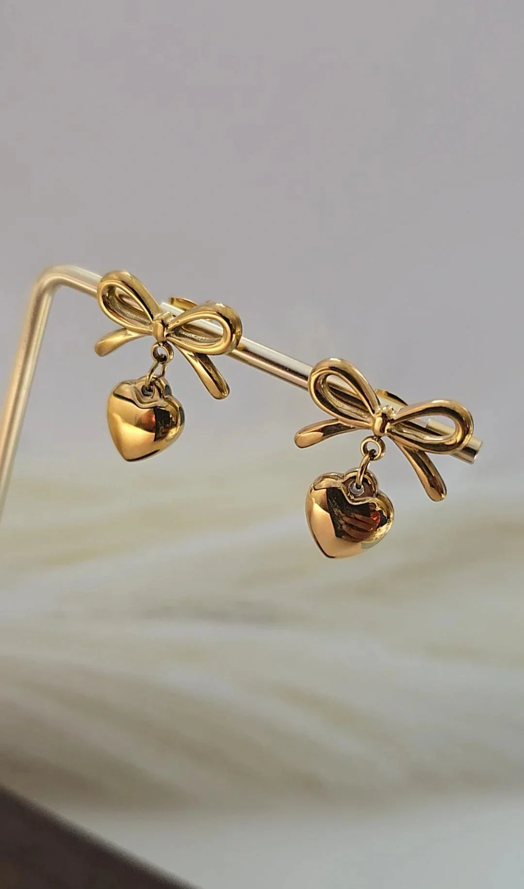 Gold bow and heart drop earrings from Bliss Bymi, elegant jewellery on display stand