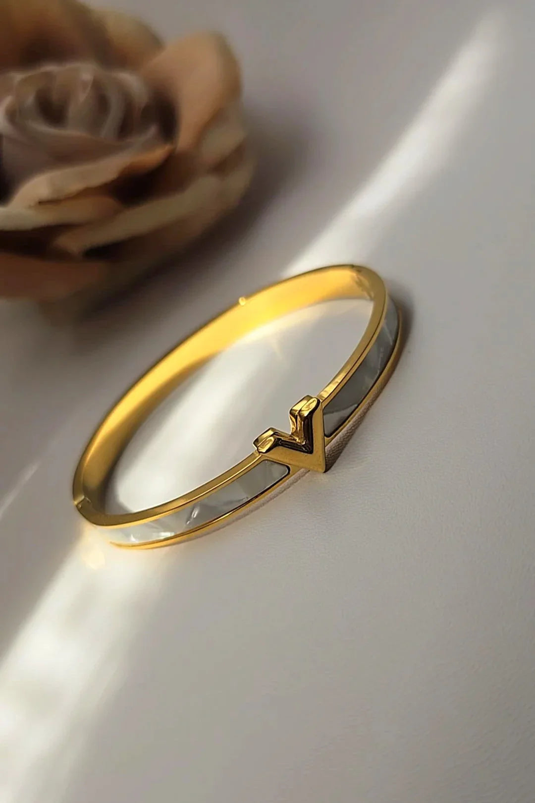 Gold and white V-shaped bangle bracelet on light surface, Bliss Bymi jewelry product