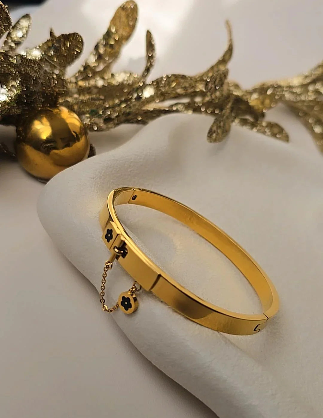 Elegant gold bracelet with black flower charms on a white cloth, Bliss Bymi jewelry.