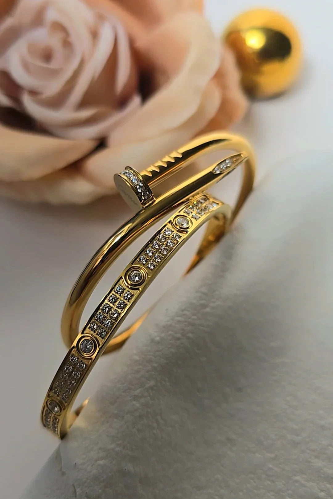 Gold bracelets with sparkling stones on a soft surface, rose and gold ball in background, Bliss Bymi jewelry.
