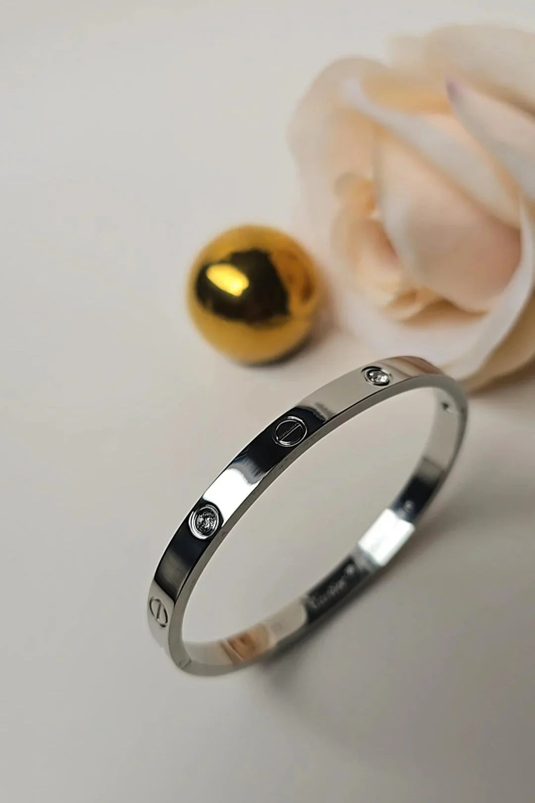Silver bracelet with gemstone accents on white surface, gold sphere and rose nearby, Blissbymi jewelry