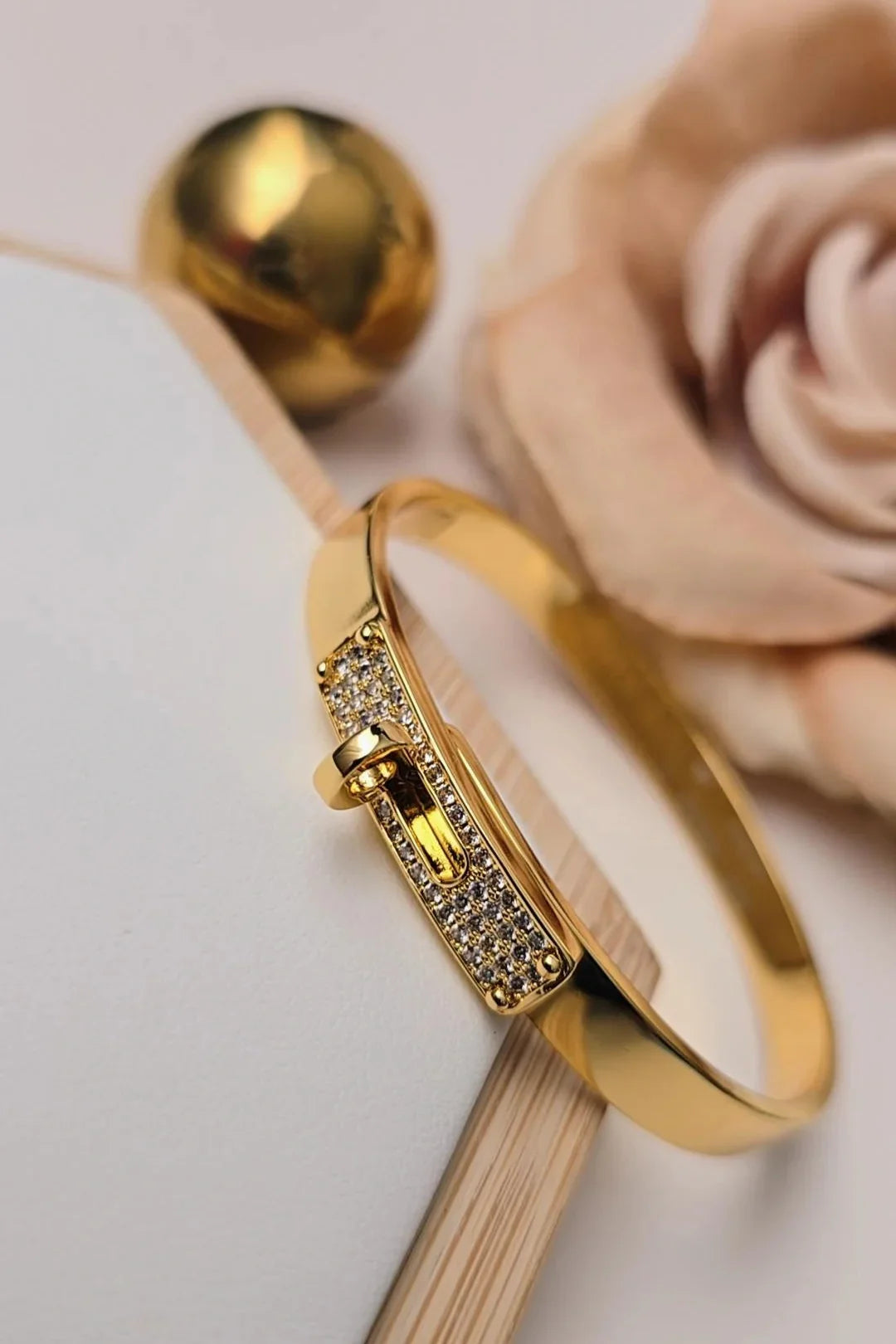 Gold bracelet with crystal accents from Bliss Bymi, styled on a soft beige background.