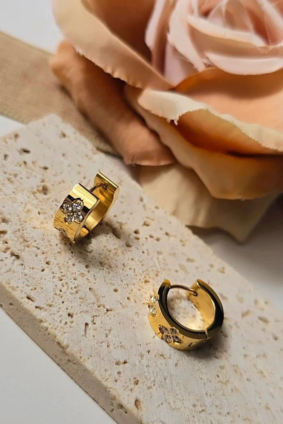 Gold hoop earrings with crystal flower accents on stone, blush rose in background from Bliss Bymi