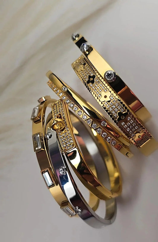 Stack of gold and silver Bliss Bymi bracelets with crystal and floral designs on a light background