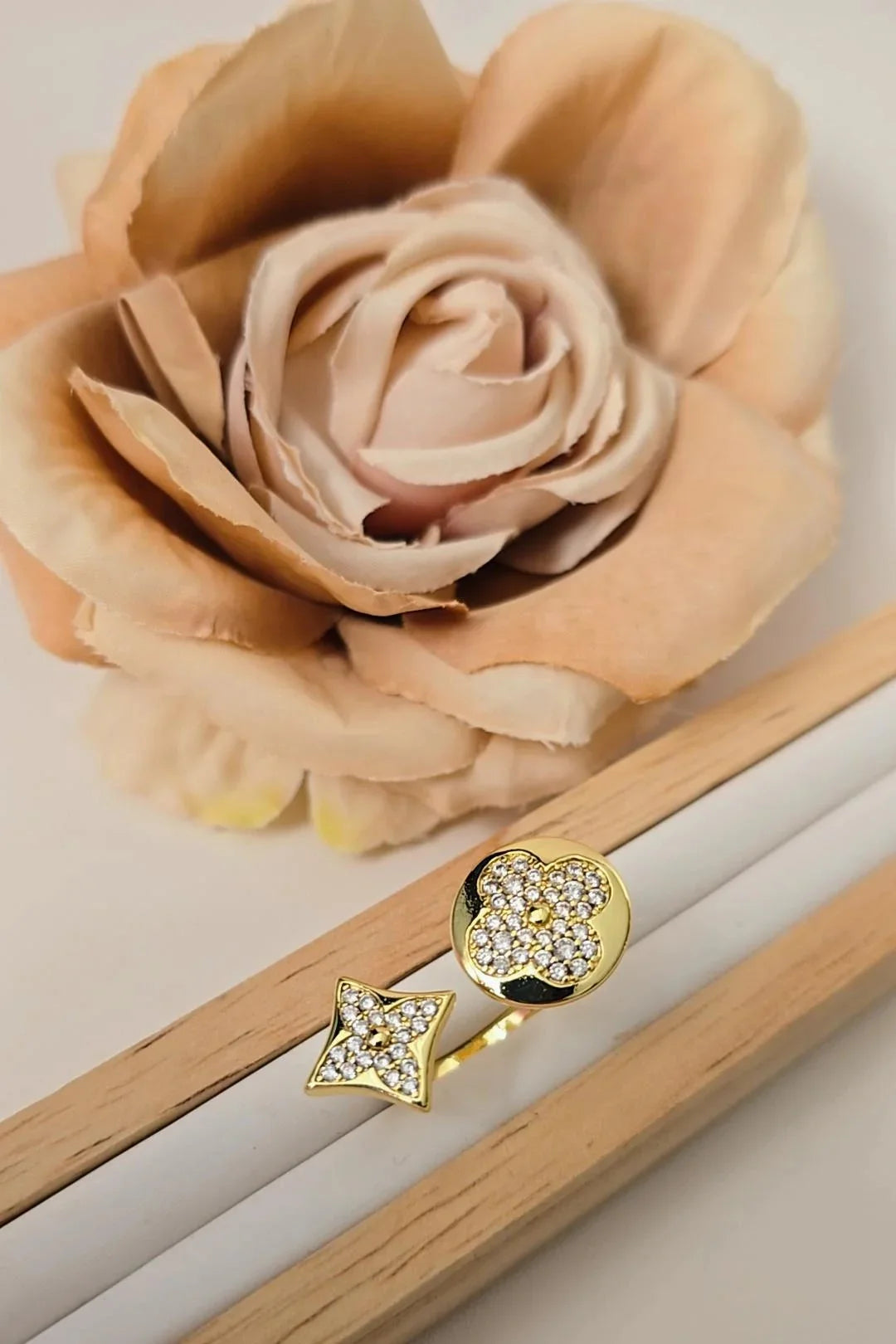 Gold Blissbymi ring with crystal star and flower design, displayed near a beige rose.