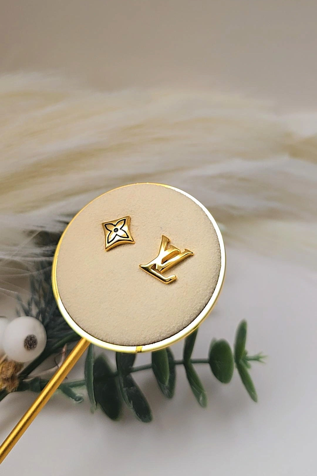 Gold earrings on a branded earring display with feathers and greenery in the background