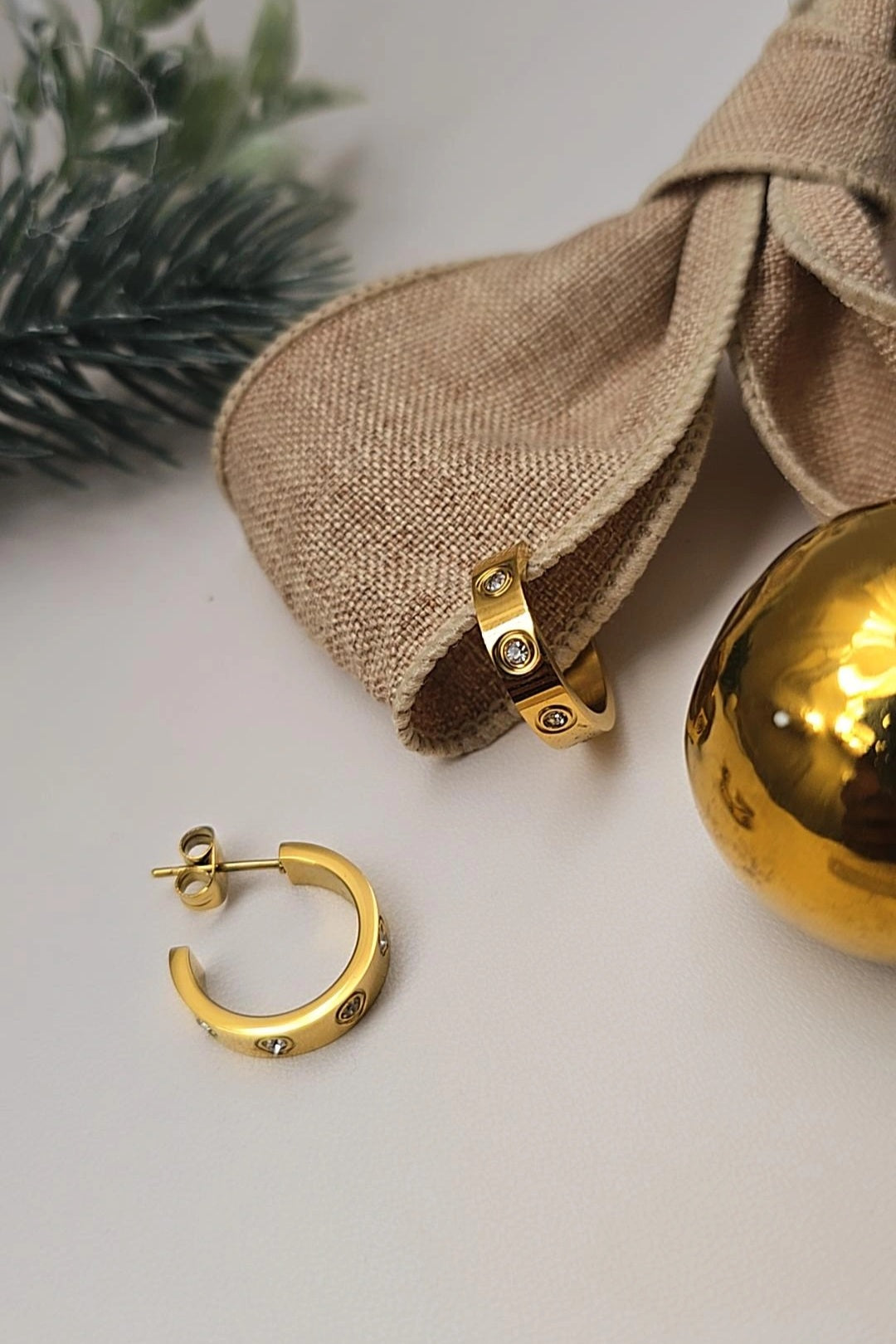 Gold hoop earrings on a light surface with a beige fabric bow and gold ornament.