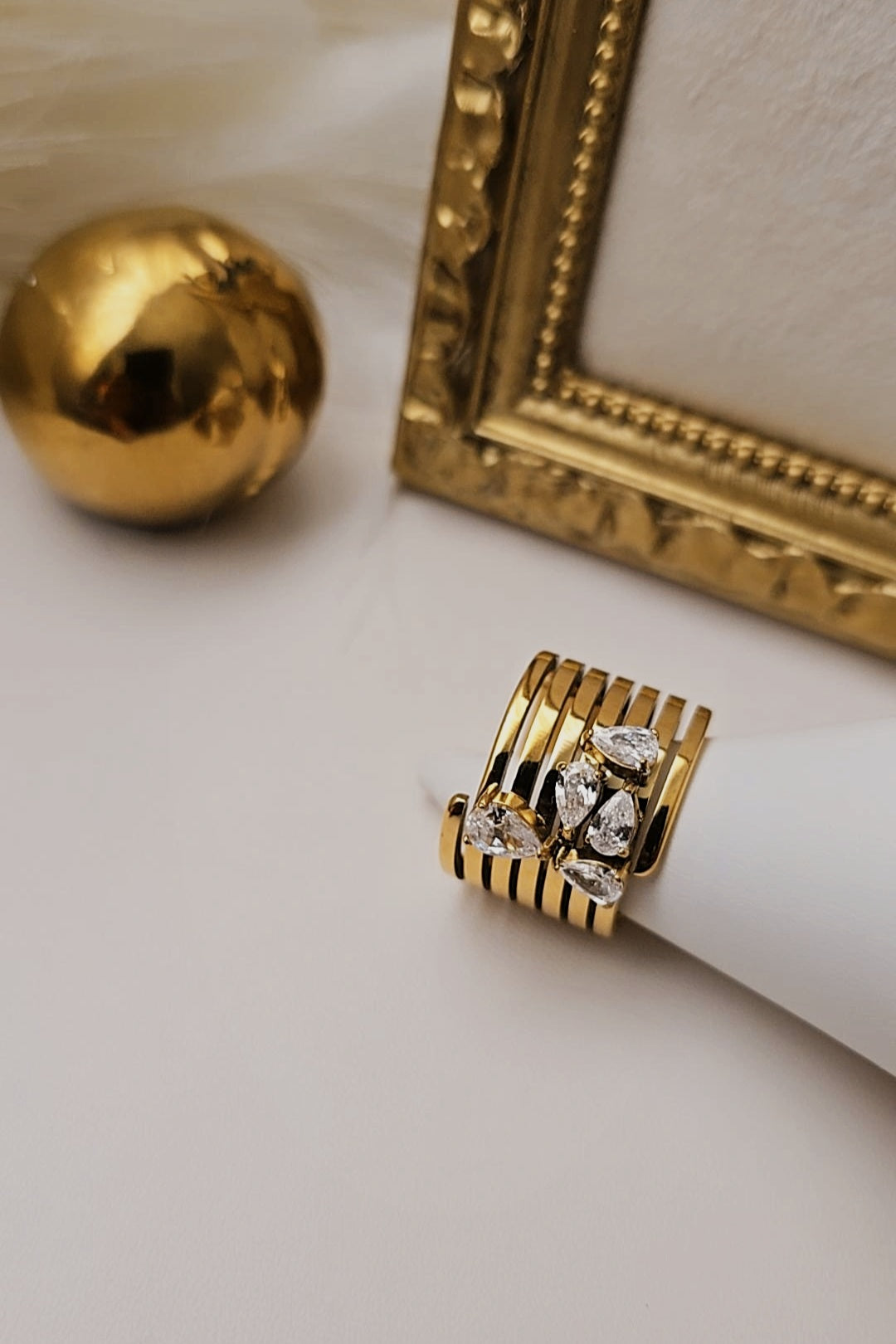 Gold ring with diamonds on a light surface next to a gold frame and sphere.