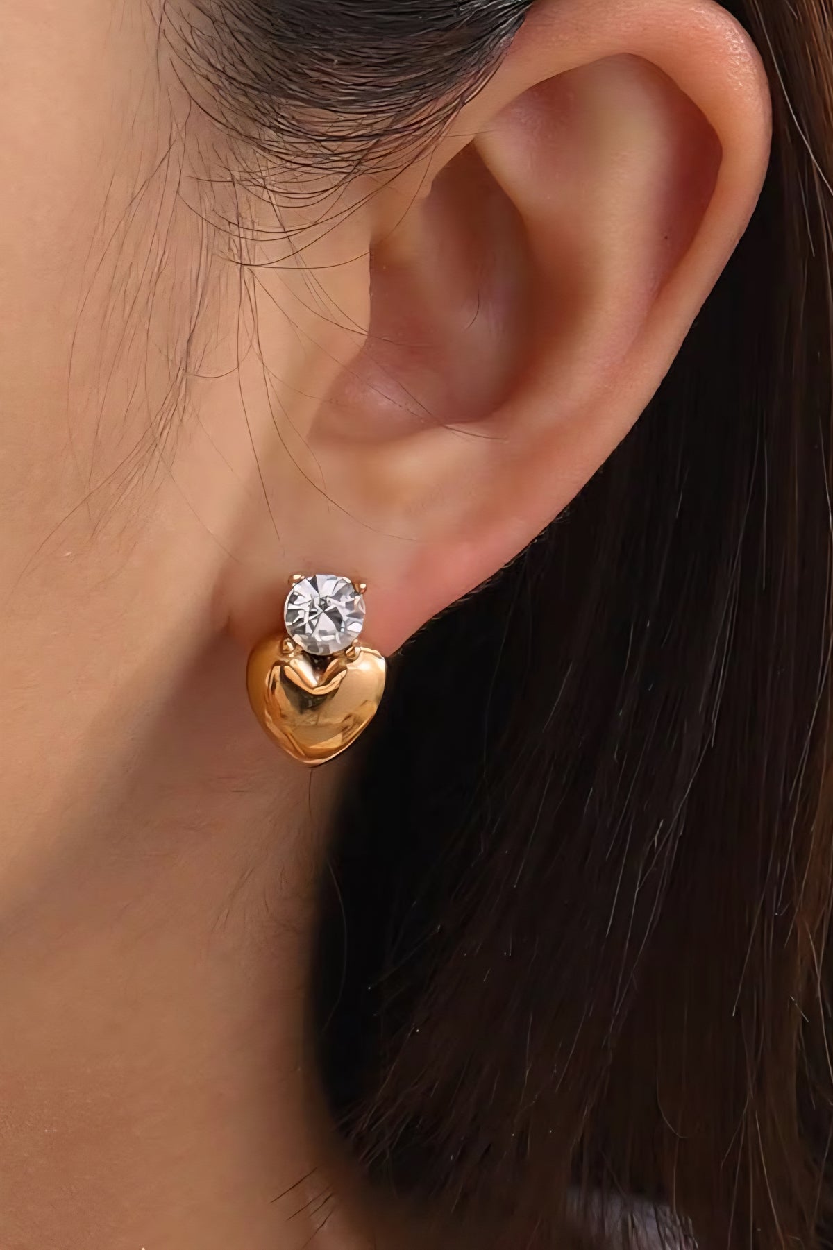 Gold heart-shaped earring with a clear gemstone worn by a person.